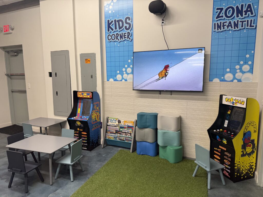LaundryJack kids’ corner with child-sized tables, books, cushioned seating, a TV, and arcade games.